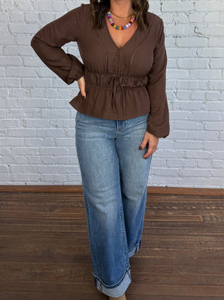 Woman wearing a brown V-neck blouse with jeans and taupe boots.