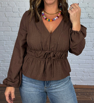 Woman wearing a brown V-neck blouse with jeans and taupe boots.