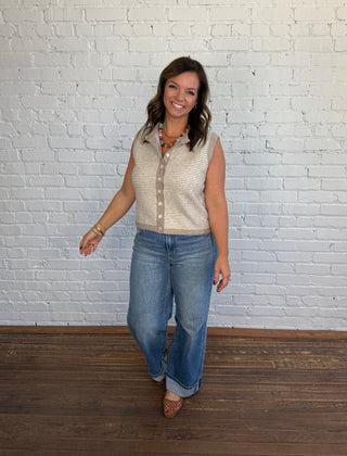 Women wearing a cream and taupe sweater vest paired with cuffed jeans and brown shoes