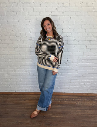 Women wearing a cream, black and blue sweater paired with denim jeans and brown flats.