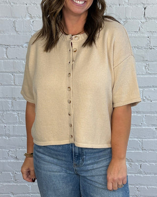 Woman wearing a button up short sleeve sweater with denim and brown shoes.