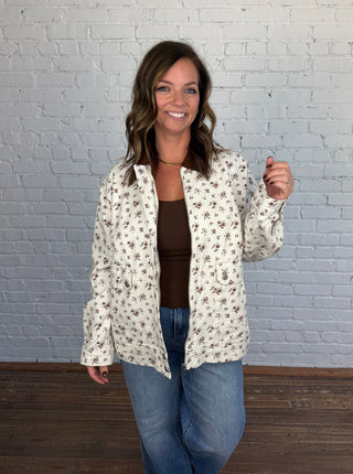 Woman wearing a cream floral jacket with a brown top jeans and taupe boots.