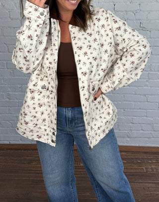 Woman wearing a cream floral jacket with a brown top jeans and taupe boots.