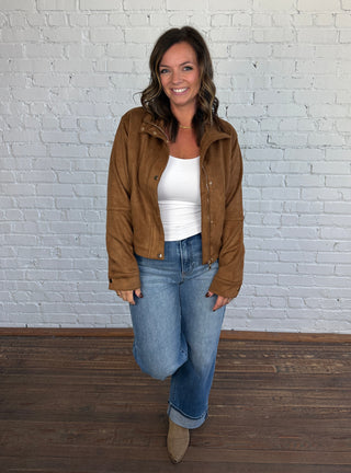 Women wearing a white top with brown jacket and medium wash denim paired with taupe boots.