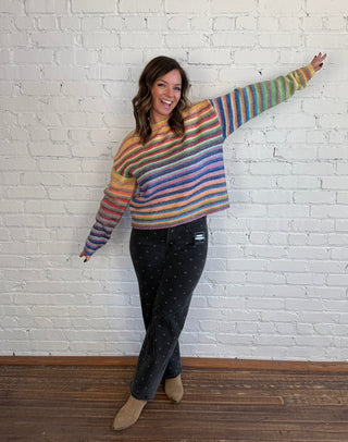 Women wearing black jeans with gray polka dots and colorful striped sweater paired with tan boots.