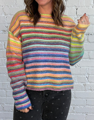 Woman wearing a colorful striped sweater, paired with black denim with gray polkadots and top boots.