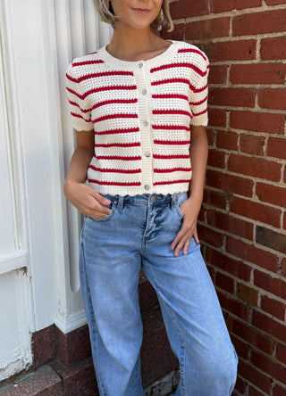 Woman wearing a red and white striped sweater and blue jeans standing against a brick wall.