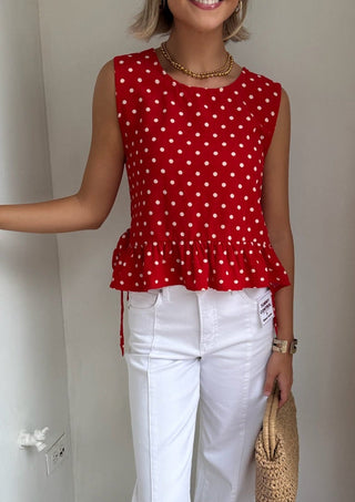 Woman wearing a red polka dot top and white pants standing in a doorway.