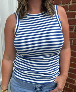 Person wearing a blue and white striped tank top and jeans standing against a brick wall.