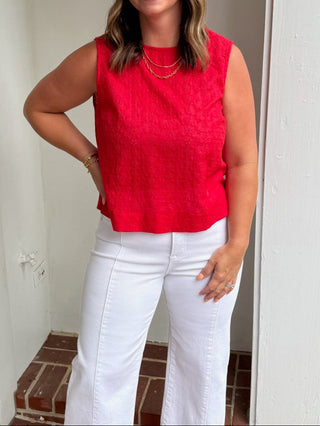 Woman in a red top and white pants standing outside a building.