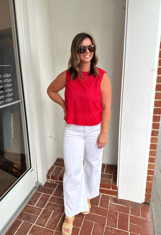Woman in a red sleeveless top and white pants standing outside a store.